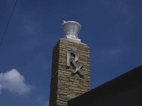 A stone pharmacy chimney carved with “Rx” against a blue sky